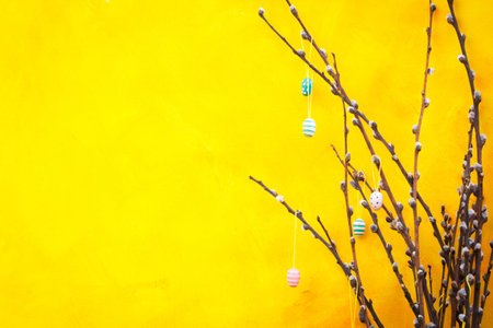 Easter yellow background with eggs hanging on branches of pussy willow.