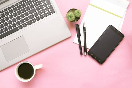 Pink office desk with laptop, smartphone, notebook, cap of coffee and cactus. Top viewの写真素材