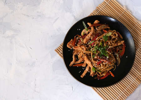Udon noodle with chicken and vegetables on the black plate with soy sauce on the bamboo serving mat on the white backgroundの写真素材