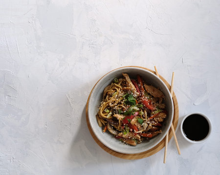 Udon bowl with chicken breast and vegetables top view with soy sauce and sticks. Asian food. Place...