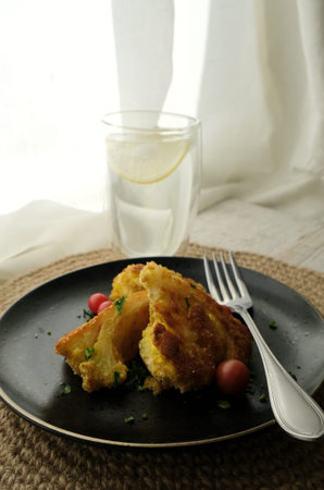 Roasted cauliflower with tomato cherries and fresh parsley on the black plate with a glass of water....