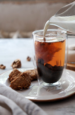 Cozy homemade oatmeal cookies and a tea in the double bottom glass and pouring milk. English tea....