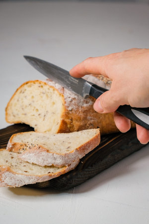 White bread on the dark wooden cutting board with hand, holding knife. Vertical photo.