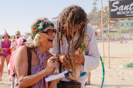 An unidentified older woman writes something in a notebook under dictation at the annual festival of Freaks, Arambol beach, Goa, India, February 5, 2013  Tourists put on crazy homemade costumes and show funny performances on the beach のeditorial素材