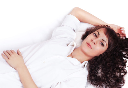 Beautiful young woman in white shirt lying on a bedの写真素材