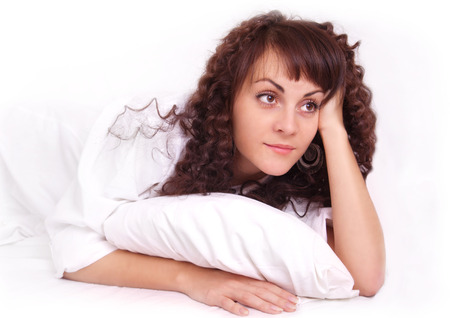 Beautiful young woman in white shirt lying on a bedの写真素材