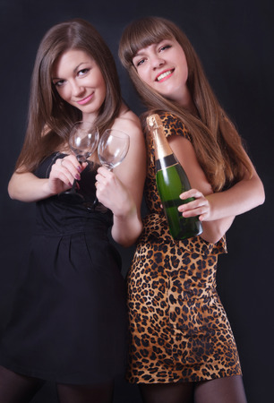 Two cheerful girls with champagne and glasses on a black backgroundの写真素材