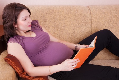 Attractive young pregnant woman reading a bookの写真素材