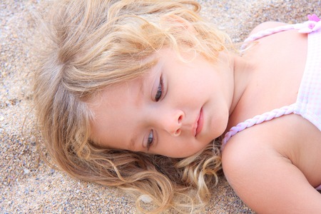 Little girl lying on the sand, on the beachの写真素材
