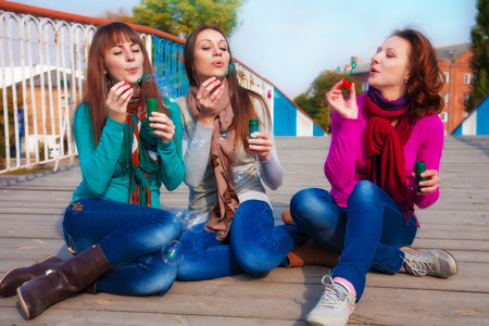 Three young beautiful women blow bubbles outdoorsの写真素材