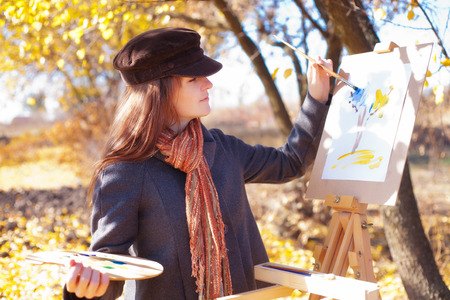 Girl with palette in hand sketches on white paperの写真素材