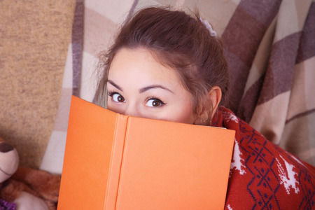 Cute girl on the sofa with a book in handの写真素材