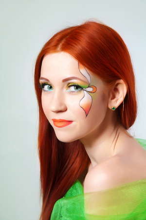 Portrait of beautiful red-haired girl with a flower painted on his faceの写真素材