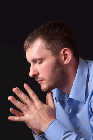 Thoughtful young man in a blue shirt, portrait on black backgroundの写真素材