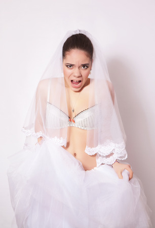 Studio portrait of beautiful angry bride wearing in a white skirt and veil, against gray backgroundの写真素材