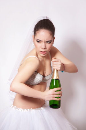 Sad bride with a bottle of champagne in hand, dressed in underwear and skirtの写真素材