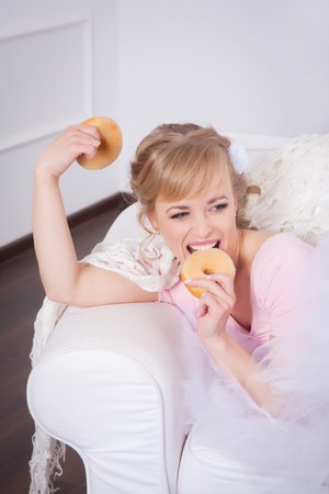 Beautiful woman sitting with a donut in his hand in a white chairの写真素材