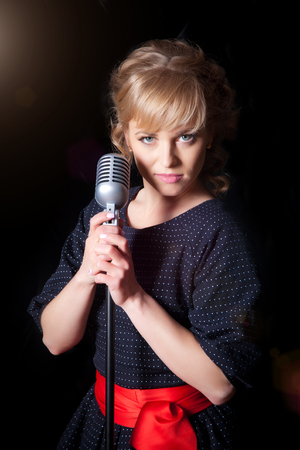 A beautiful girl with a microphone on stage, black backgroundの写真素材