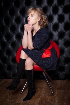 Woman in black dress sitting on a red chair, studio shotの写真素材