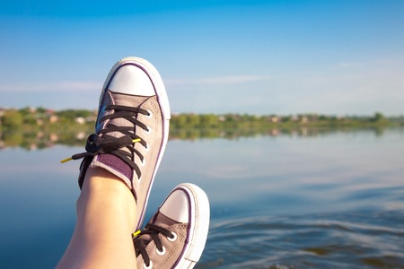 Female feet in sneakers on the background of a river landscape sunny summer dayの写真素材