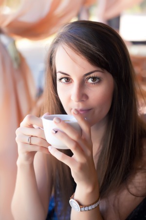 Close-up portrait of a beautiful woman with a cup of coffee at a cafeの写真素材