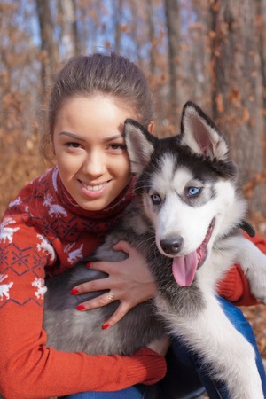 Beautiful young woman hugging huskies puppy for a walk in the park in autumnの写真素材