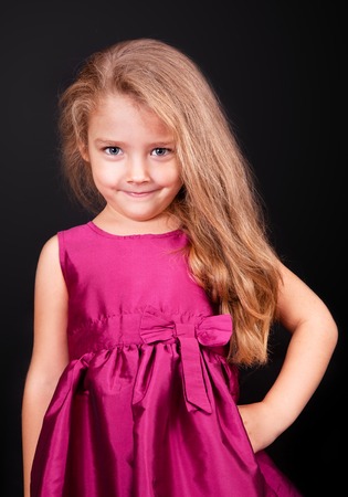 Little cute girl in a pink dress on a black background in the studioの写真素材