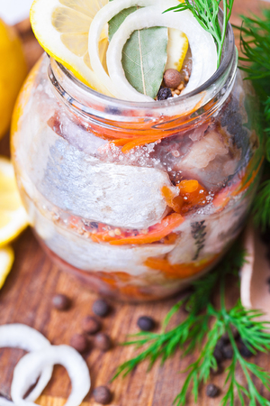 Marinated herring in a jar with vegetables and herbsの写真素材