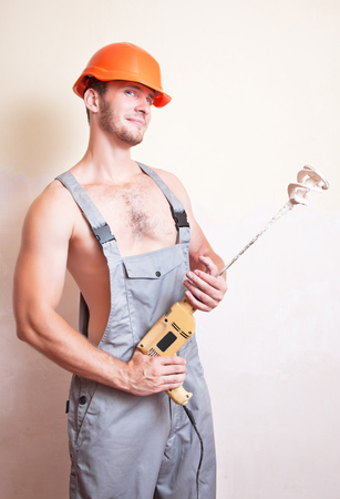 A man in overalls and helmet with a mixer for plasteringの写真素材