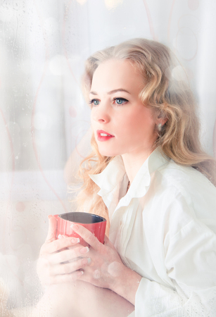 The woman at the window on a rainy day with a cup in her handsの写真素材