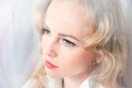 Close-up portrait of a sad beautiful woman near the window on a rainy dayの写真素材