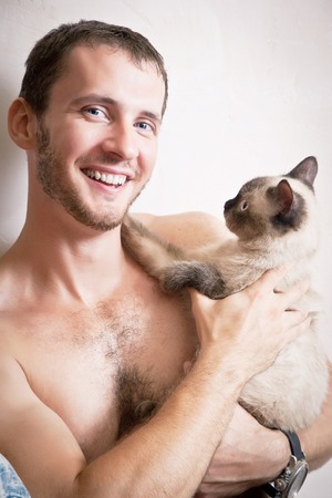 Portrait of a young attractive smiling man with a cat in hands, studio shootingの写真素材