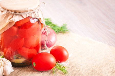 Canned tomatoes with garlic and herbs in a glass jar on the wooden tableの写真素材