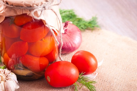 Canned tomatoes with garlic and herbs in a glass jar on the wooden tableの写真素材