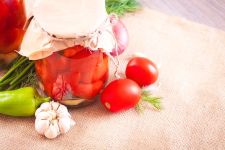 Canned tomatoes with garlic and herbs in a glass jar on the wooden tableの写真素材