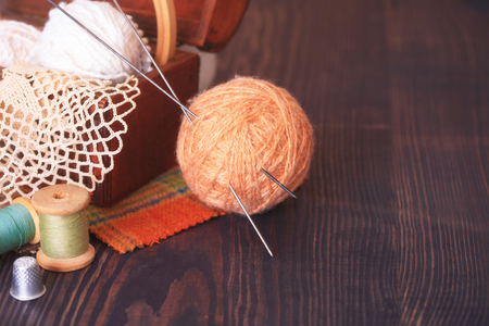 Casket with needlework and beige skein of thread with spokes for knitting on a wooden tableの写真素材