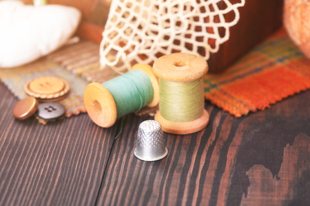 Spool of thread, a thimble and a box with needlework on a wooden table close-upの写真素材