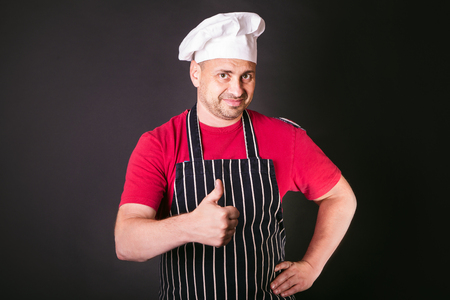 Portrait of a cook man doing a success symbol against a black backgroundの写真素材