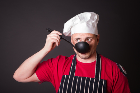 Portrait of a funny cook with a ladle in his hand in the studio on a black backgroundの写真素材