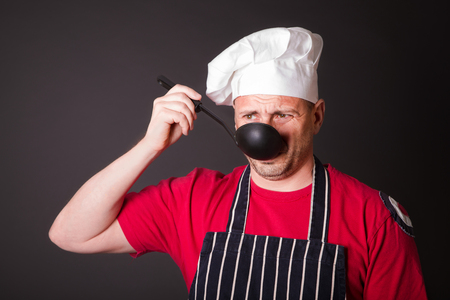 Portrait of a funny cook with a ladle in his hand in the studio on a black backgroundの写真素材
