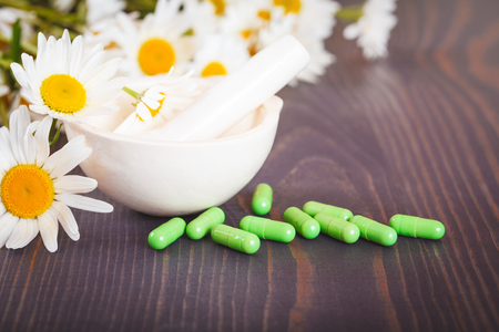 Chamomile flowers and green phytotherapeutic capsules on a wooden table. Herbal medicine and healthの写真素材