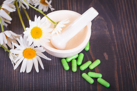 Chamomile flowers and green phytotherapeutic capsules on a wooden table. Herbal medicine and healthの写真素材