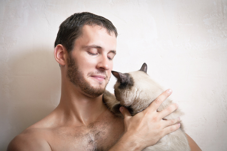 Portrait of a young attractive smiling man with a cat in hands, studio shootingの写真素材