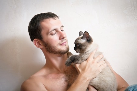 Portrait of a young attractive smiling man with a cat in hands, studio shootingの写真素材