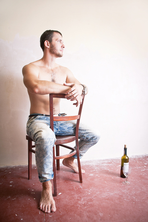 Man with a bottle of wine sitting on a chairの写真素材