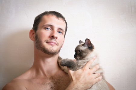 Portrait of a young attractive smiling man with a cat in hands, studio shootingの写真素材