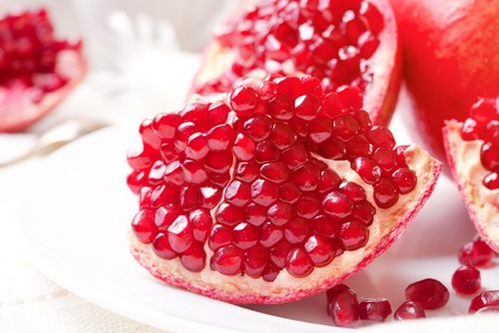 Piece of juicy ripe pomegranate on a white plate closeupの写真素材