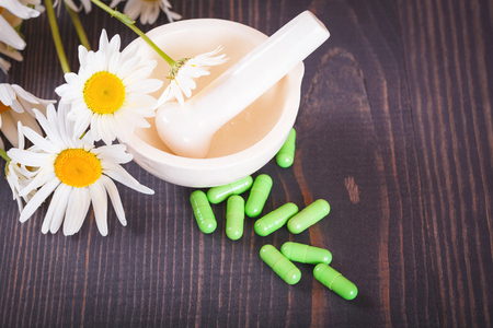 Chamomile flowers and green phytotherapeutic capsules on a wooden table. Herbal medicine and healthの写真素材
