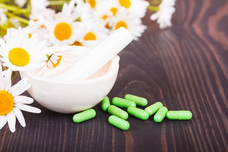 Chamomile flowers and green phytotherapeutic capsules on a wooden table. Herbal medicine and healthの写真素材