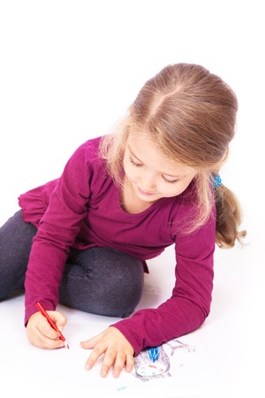 Little cute girl draws pencils sitting on the floor on a white backgroundの写真素材